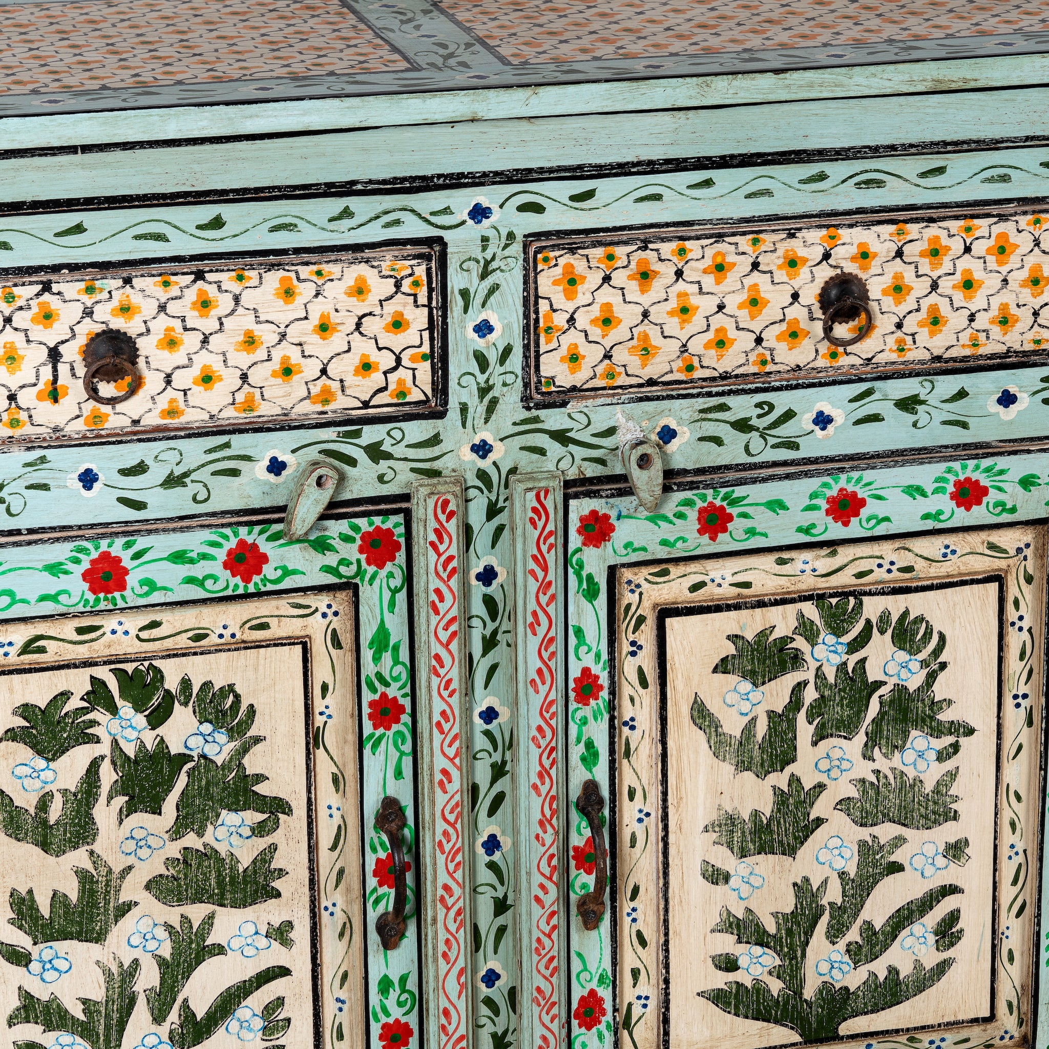 Close up image of a hand-painted sideboard made from reclaimed wood, featuring three drawers and three cabinet doors adorned with intricate floral borders and tree motifs in earthy green and warm tones, finished in a soft distressed patina for a vintage artisanal look.
