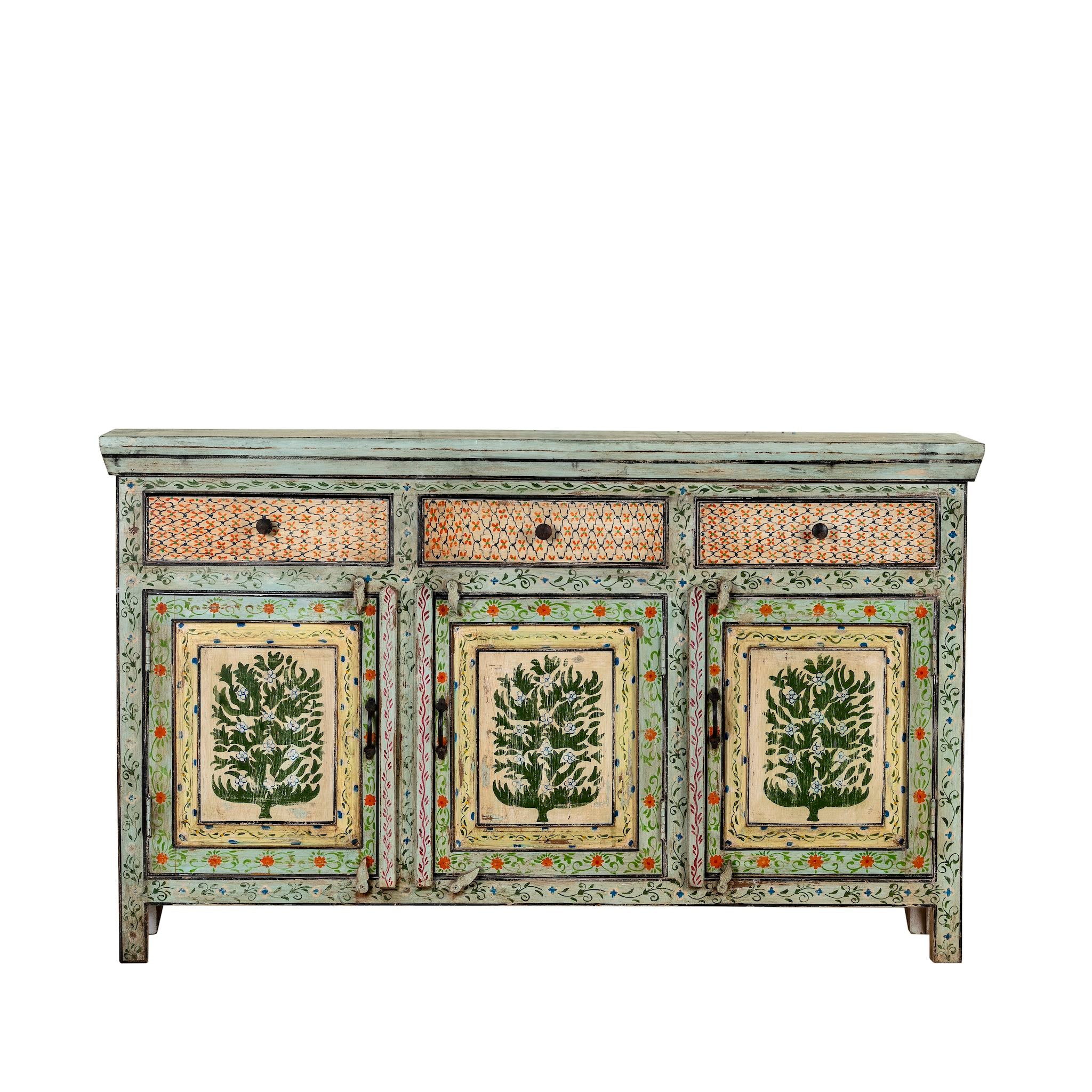 White background image of a hand-painted sideboard made from reclaimed wood, featuring three drawers and three cabinet doors adorned with intricate floral borders and tree motifs in earthy green and warm tones, finished in a soft distressed patina for a vintage artisanal look.
