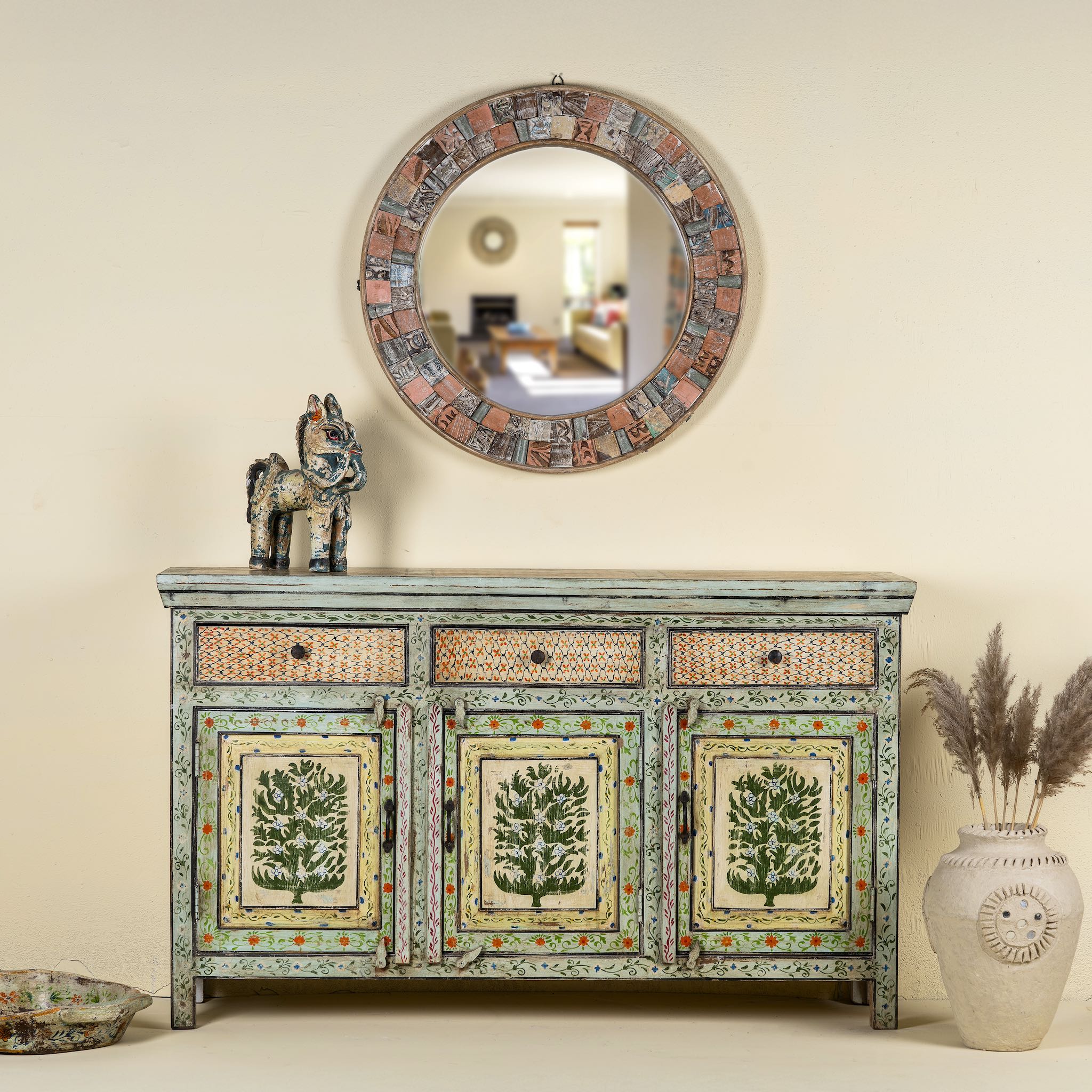 Front view image of a hand-painted sideboard made from reclaimed wood, featuring three drawers and three cabinet doors adorned with intricate floral borders and tree motifs in earthy green and warm tones, finished in a soft distressed patina for a vintage artisanal look.
