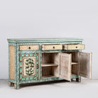 Image showing open doors of a image of a hand-painted sideboard made from reclaimed wood, featuring three drawers and three cabinet doors adorned with intricate floral borders and tree motifs in earthy green and warm tones, finished in a soft distressed patina for a vintage artisanal look.
