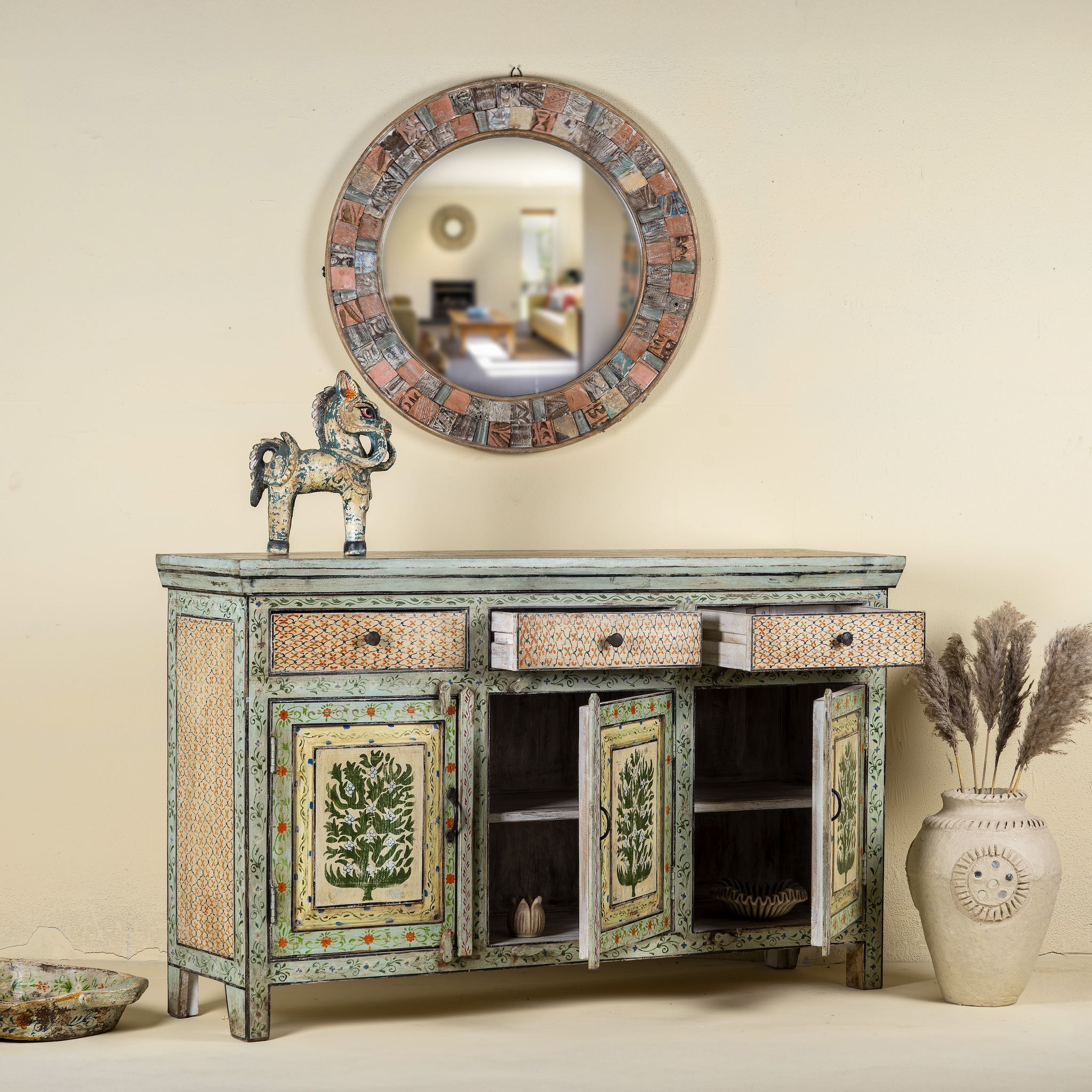 Open doors image of a hand-painted sideboard made from reclaimed wood, featuring three drawers and three cabinet doors adorned with intricate floral borders and tree motifs in earthy green and warm tones, finished in a soft distressed patina for a vintage artisanal look.
