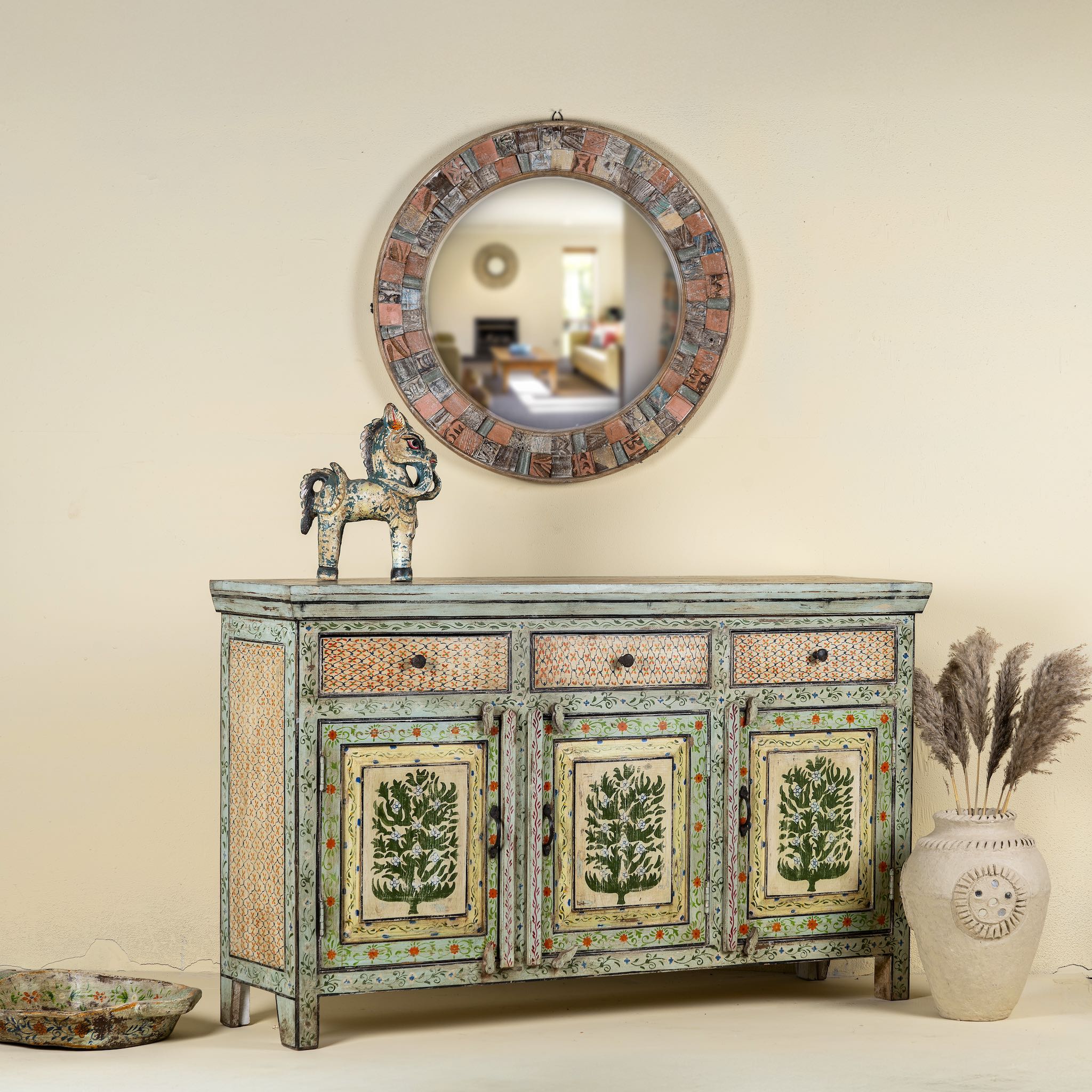 Side angle image of a hand-painted sideboard made from reclaimed wood, featuring three drawers and three cabinet doors adorned with intricate floral borders and tree motifs in earthy green and warm tones, finished in a soft distressed patina for a vintage artisanal look.

