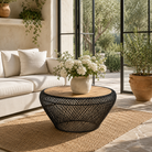Lifestyle image of a large round metal base coffee table with recycled wooden top and woven iron base; minimalistic style coffee table, 100 cm diameter, 45 cm height.
