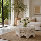 Lifestyle image of a octagonal mango wood coffee table with floral carvings and white wash finish; hand-carved and rustic, 90 × 90 × 46 cm.