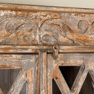 Close up image of a vintage display cabinet made from solid mango wood with glass doors and shelving – handcrafted Ibiza-style showcase with carved details.