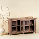 Side angle image with open doors of a reclaimed wood dresser with four glass doors, teak wood showcase cabinet with brass handles and wooden latches, 170 × 40 × 90 cm.