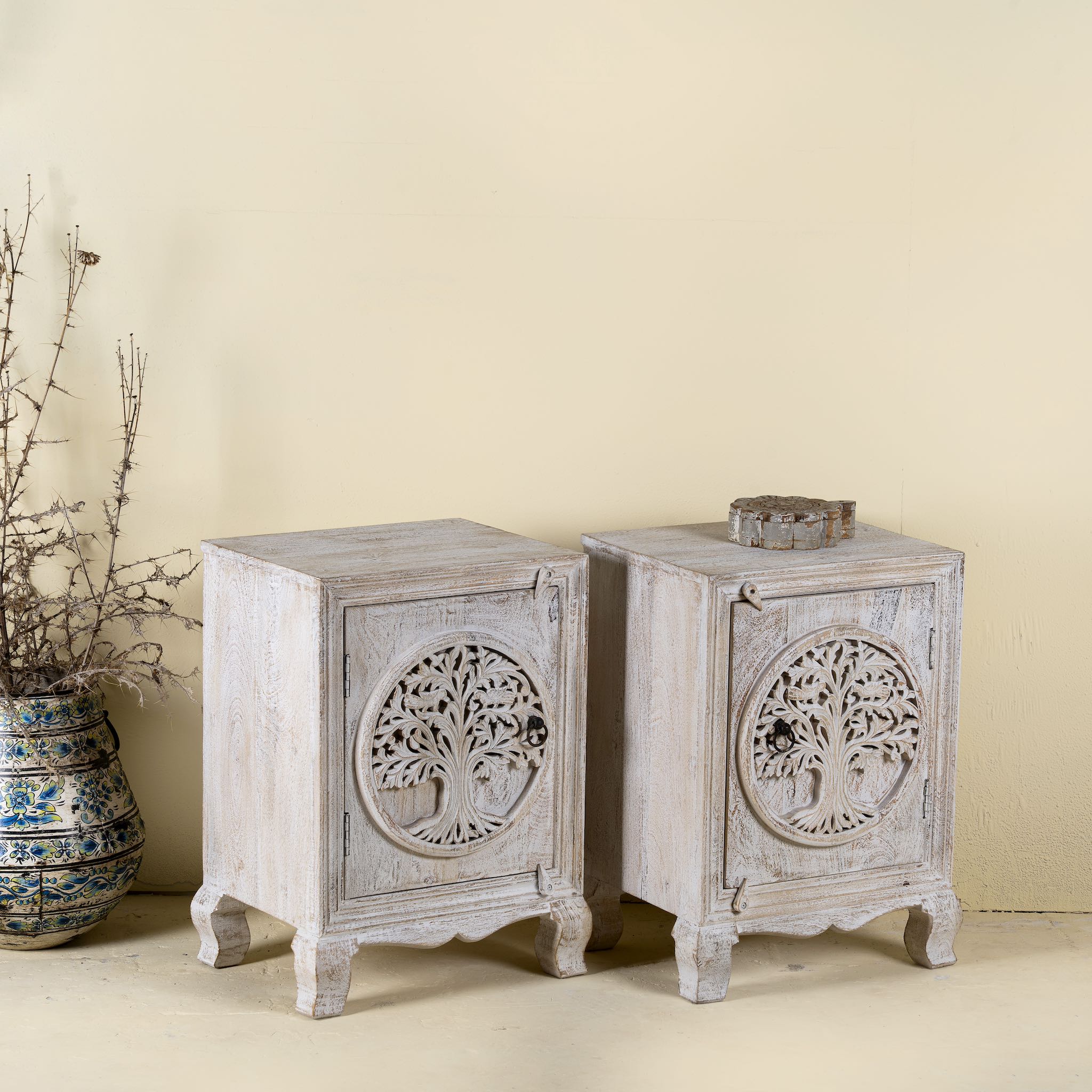 Side angle image of a pair of mango wood bedside tables with hand-carved tree motifs and antique finish; perfect bedroom furniture and mango wood furniture, 50 × 70 × 40 cm.