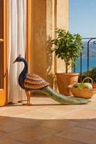 Decorative peacock sculpture on a tiled floor with a scenic view in the background
