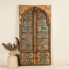 Hand-painted wooden wall panel made from an old window frame, featuring intricate blue floral patterns along with stylised animal motifs such as elephants and camels, set against a distressed golden-brown background with an arched top frame.
