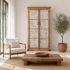 Lifestyle image of a mango wood wardrobe with whitewashed floral carvings, vintage furniture cabinet in carved wood, 190 × 105 × 42 cm.