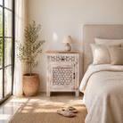 Lifestyle scene of a carved nightstand made of natural mango wood with geometric patterns and distressed finish; perfect bedroom furniture, 76 × 56 × 35 cm.
