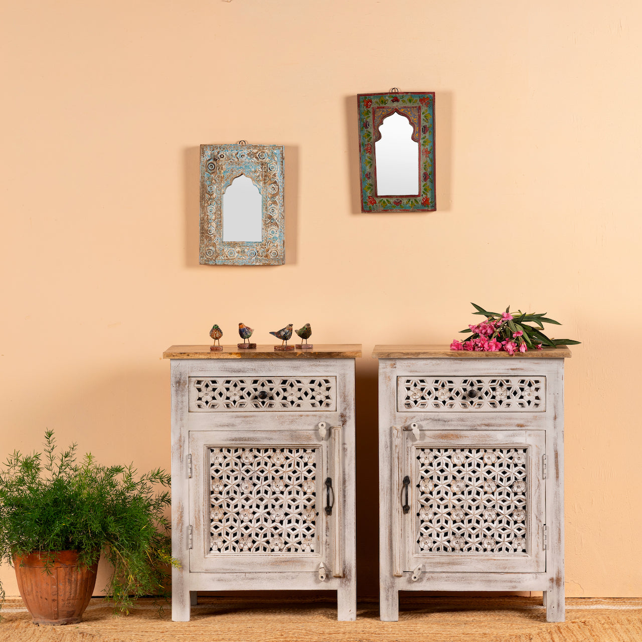 A pair of vintage style, hand-carved mango wood nightstands with geometric lattice design, light distressed finish, with plants and decorative items on top.