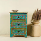 A hand-painted reclaimed wood nightstand with vibrant colours and floral patterns, featuring three drawers, placed next to a vase with dried plants.