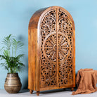 Side angle image of a unique wooden wardrobe made from solid mango wood with hand-carved floral design and rounded shape, 100 × 40 × 190 cm.
