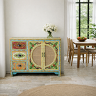 Lifestyle image of a hand painted sideboard Ashara made of mango wood with rattan inserts; Ibiza-inspired boho chic furniture, 120 × 40 × 92 cm.