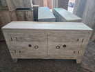 A carved light beige wooden sideboard cabinet with circular patterns on the doors and dark metal ring pulls, photographed in a showroom with other furniture pieces in the background.