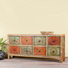 Side angle image of a hand painted sideboard with 8 drawers made of natural mango wood; artisanal chest for bohemian interior, 200 × 40 × 90 cm.