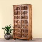 Side angle image of a hand-carved mango wood wardrobe with floral motifs; wooden wardrobe in natural finish, 100 × 45 × 190 cm.