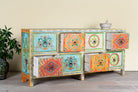 Side angle image with open drawers  of a hand painted sideboard with 8 drawers made of natural mango wood; artisanal chest for bohemian interior, 200 × 40 × 90 cm.