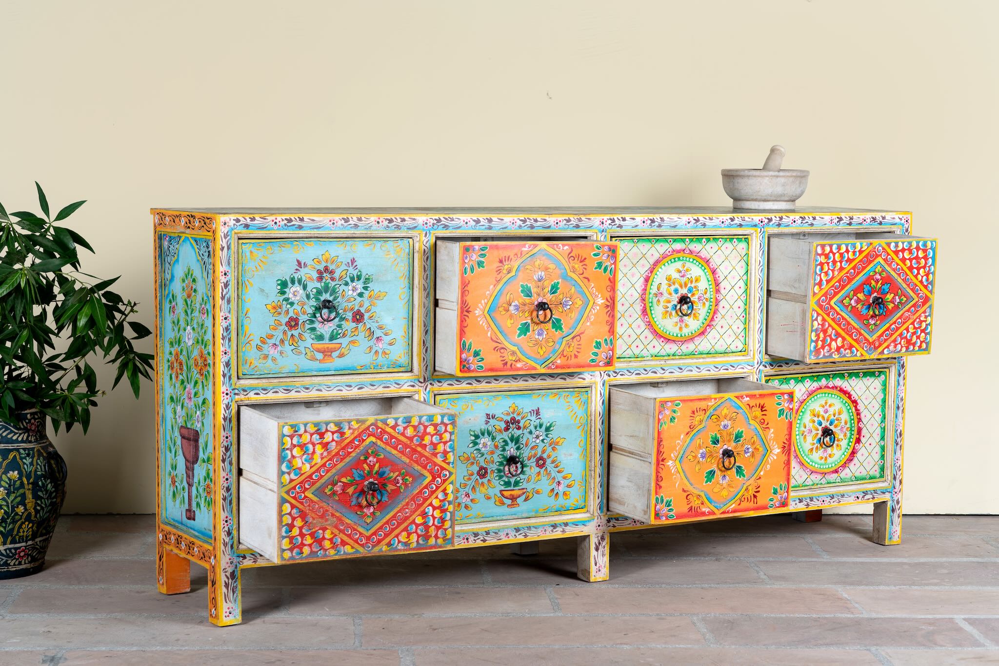 Side angle image with open drawers  of a hand painted sideboard with 8 drawers made of natural mango wood; artisanal chest for bohemian interior, 200 × 40 × 90 cm.
