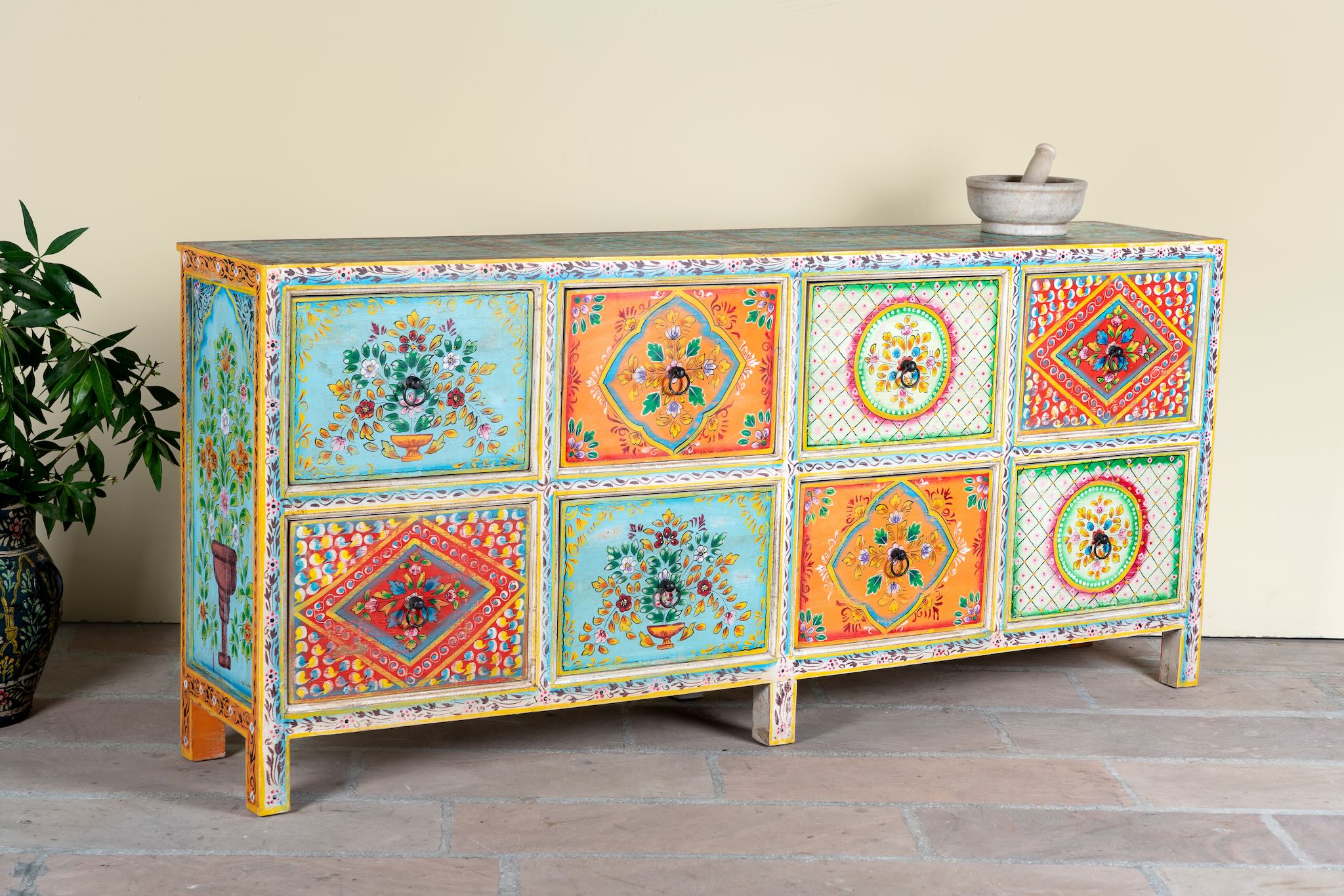 Side angle image of a hand painted sideboard with 8 drawers made of natural mango wood; artisanal chest for bohemian interior, 200 × 40 × 90 cm.