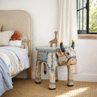 Lifestyle imagination of a hand-painted wooden cow-shaped side table with Indian script and blue folk art patterns, perfect for vintage and India-inspired home interiors.