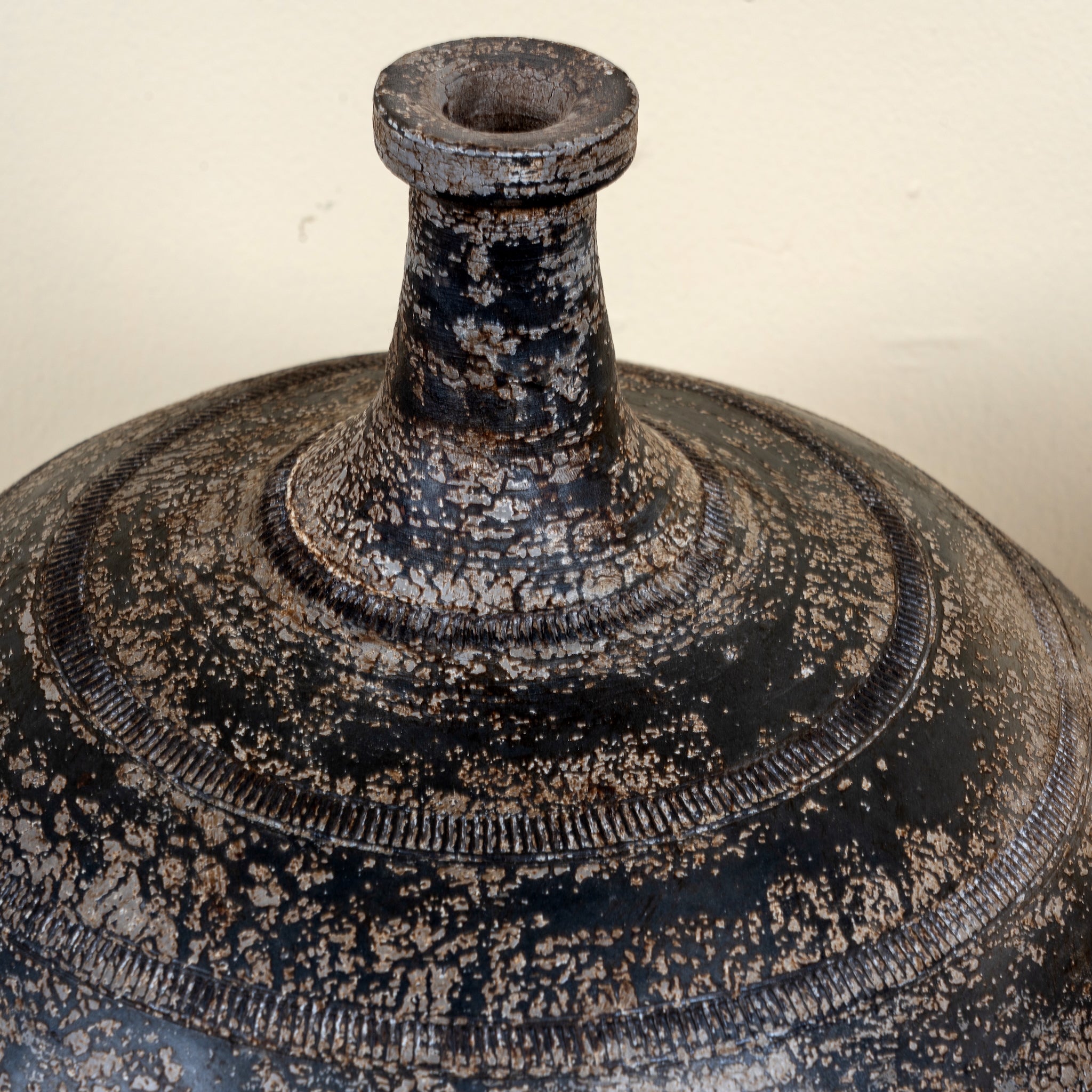 Close up image of a hand-painted clay vase with rounded body, narrow neck and iron stand, handcrafted decorative vase with rustic aged finish, 40cm.