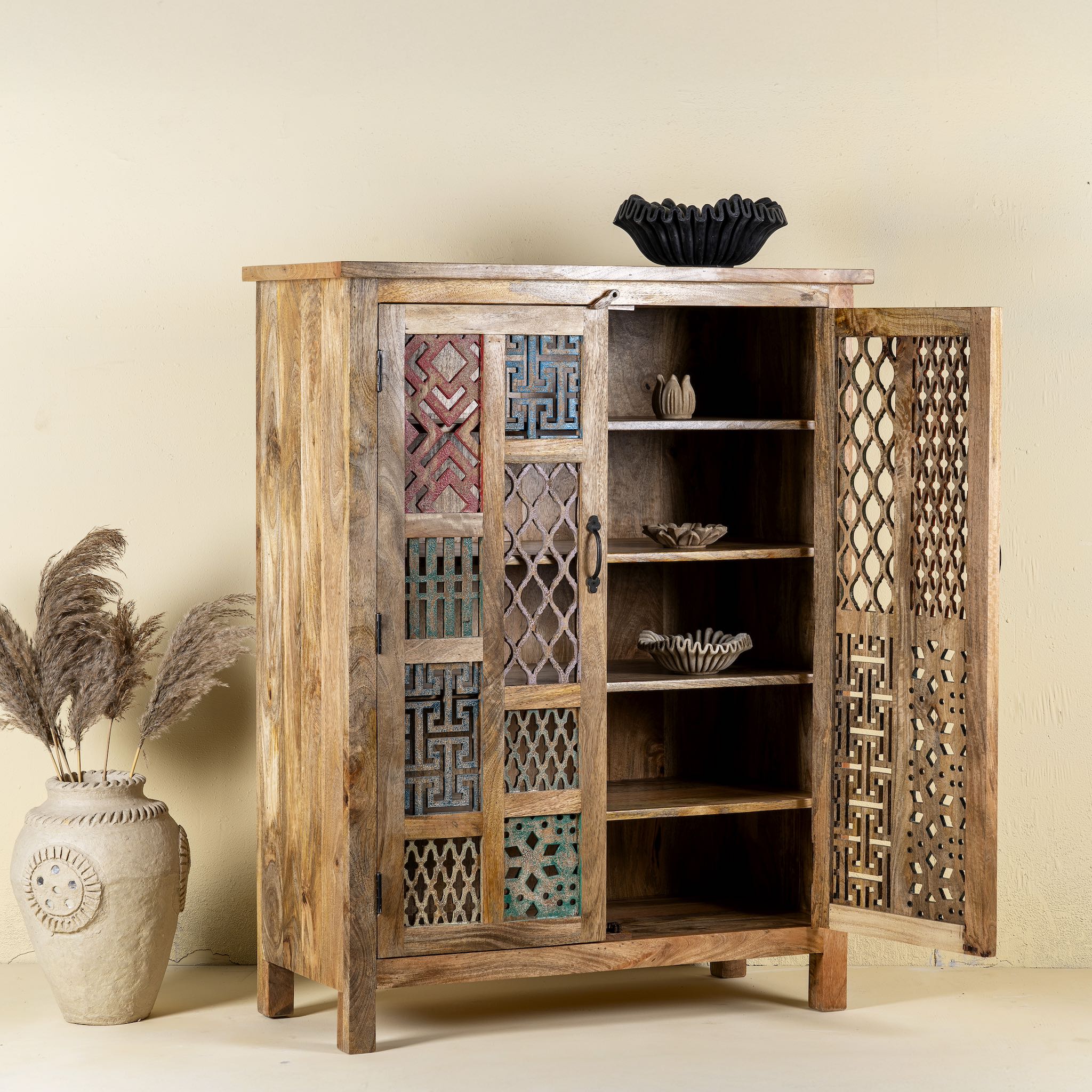 Side angle with open door image  of a artisanal mango wood cabinet with hand-carved floral and geometric lattice doors, distressed finish; ideal for boho style interiors, 100 × 45 × 130 cm.