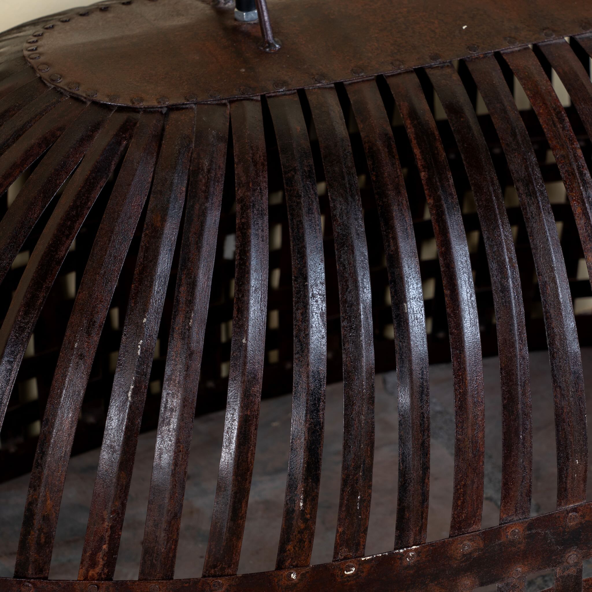 Close up image of a Chitra metal pendant light with hand-forged slatted design and iron chain suspension—an artisanal example of hand crafted metal lamps and bold metal pendant lights for high ceilings.