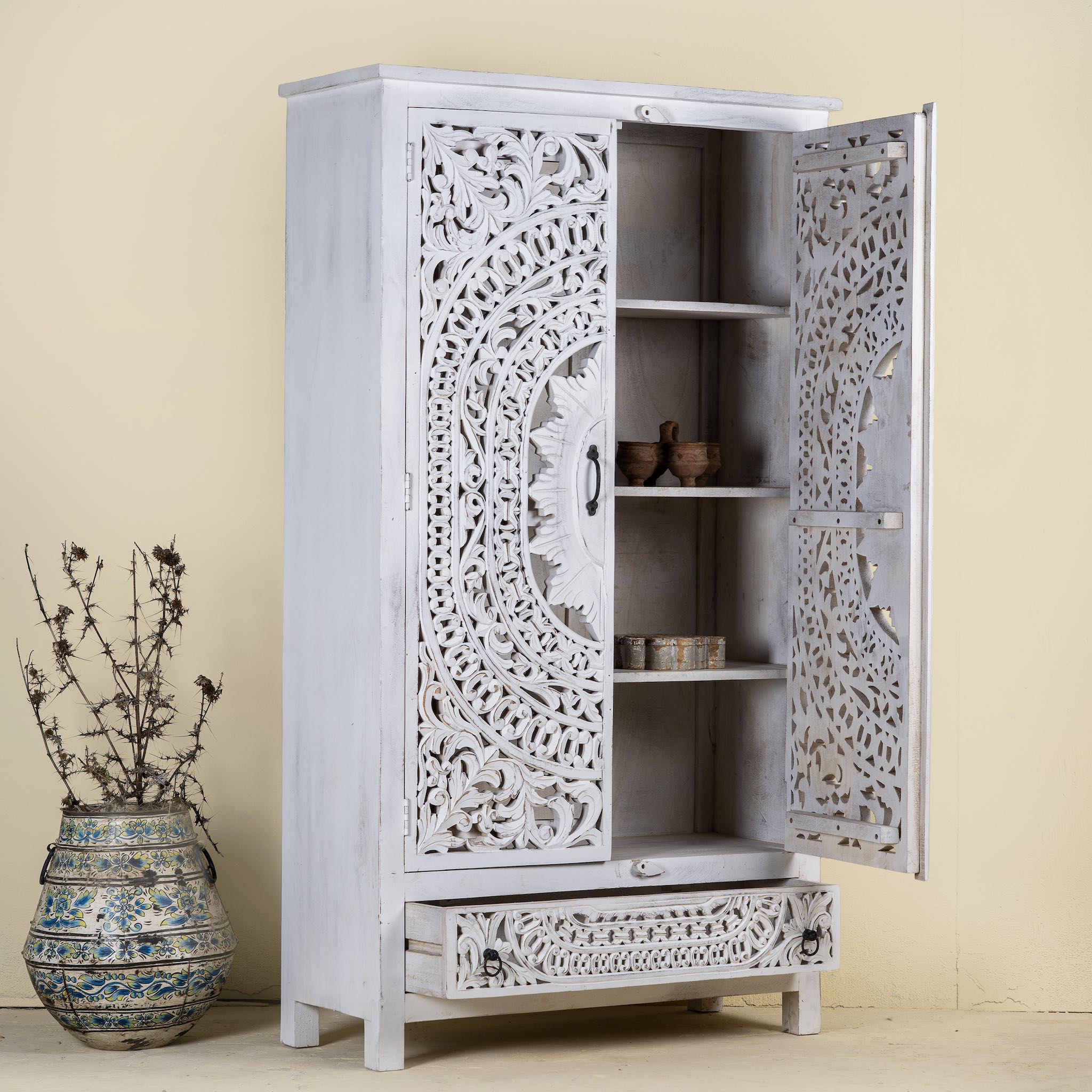 Open door image of a hand-carved mango wood wardrobe with floral and geometric patterns and white-washed finish – carved wooden furniture for boho chic and Mediterranean-inspired interiors.