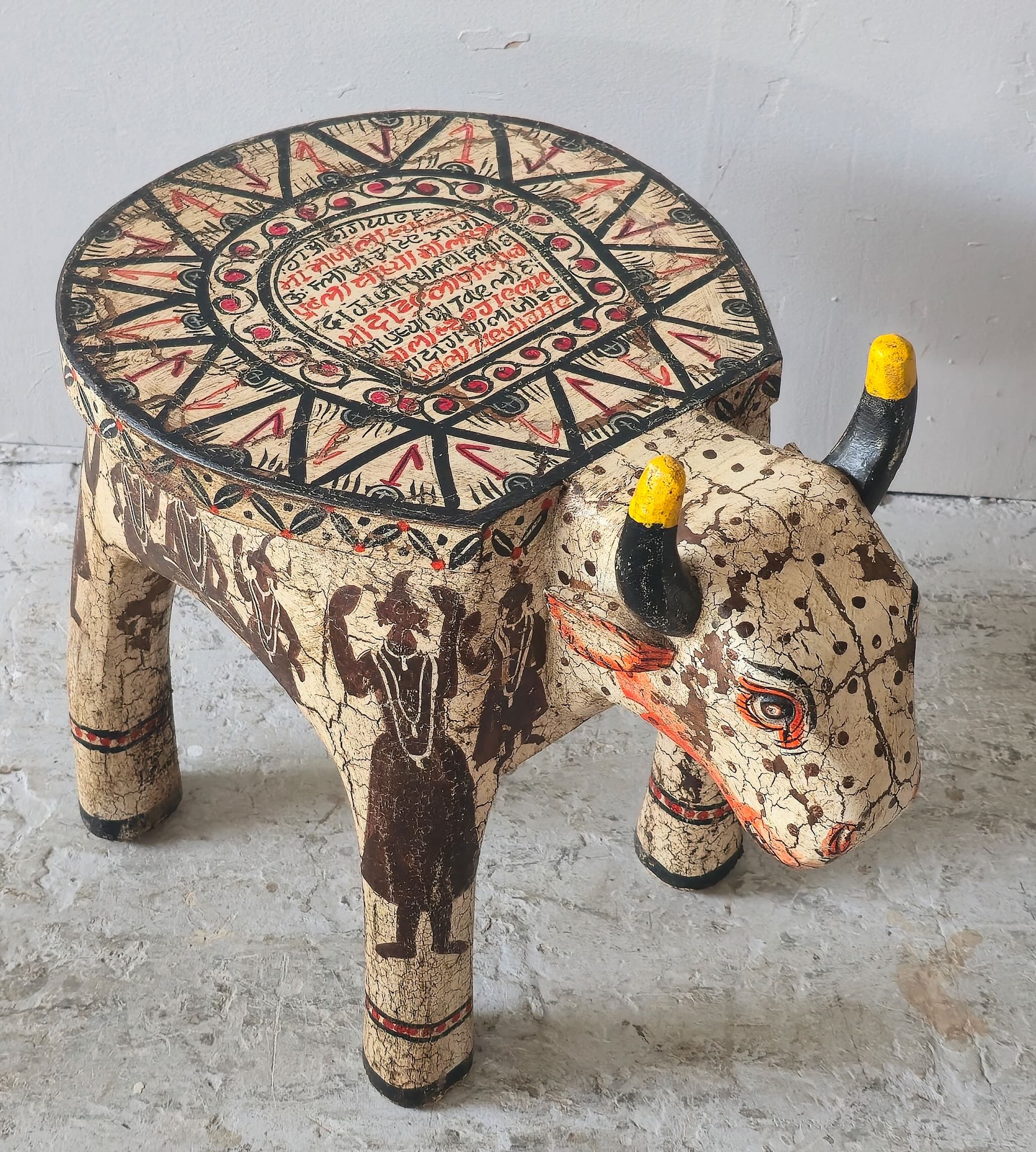 Hand-painted wooden cow-shaped side table with Indian script and blue folk art patterns, perfect for vintage and India-inspired home interiors.