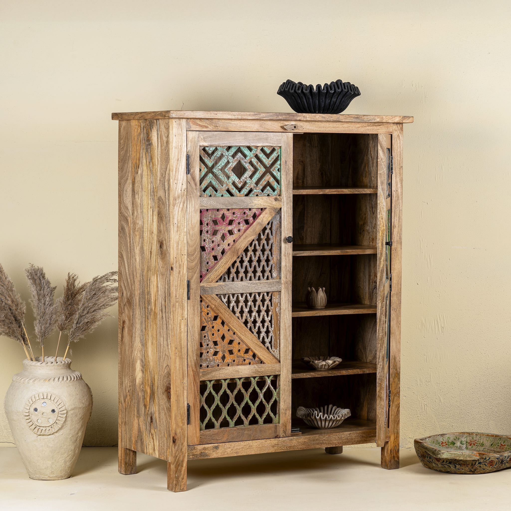 Side angle image with open door of a  handmade mango wood cabinet with carved floral and geometric lattice doors, distressed colour accents; artisanal furniture perfect for boho style interiors, 100 × 45 × 130 cm.
