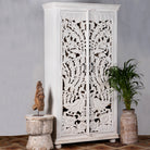 Side angle image of a hand-carved mango wood wardrobe with peacock and floral motifs, whitewashed finish; elegant wooden wardrobe and mango wood furniture, 190 × 100 × 40 cm.