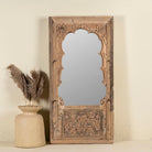 Hand-carved mirror crafted from an old teak wood window frame, featuring intricate floral and scrollwork details with a natural distressed finish and an arched top design reflecting traditional Indian craftsmanship.
