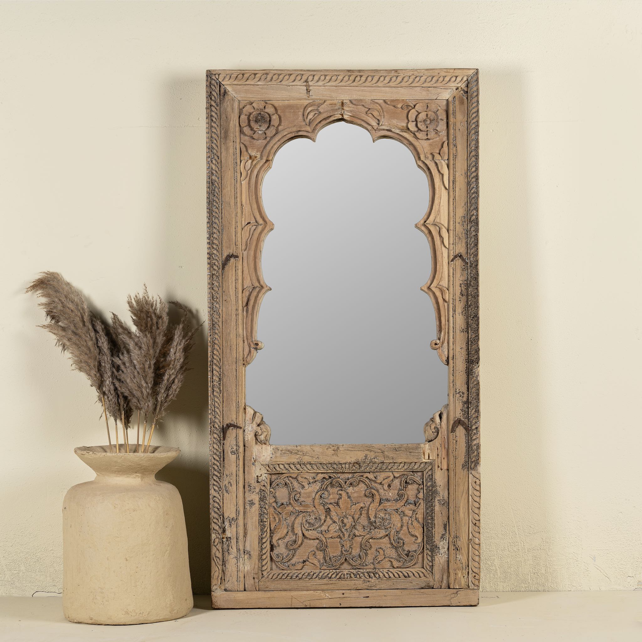 Hand-carved mirror crafted from an old teak wood window frame, featuring intricate floral and scrollwork details with a natural distressed finish and an arched top design reflecting traditional Indian craftsmanship.
