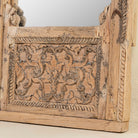 Close up of the base of a hand-carved mirror crafted from an old teak wood window frame, featuring intricate floral and scrollwork details with a natural distressed finish and an arched top design reflecting traditional Indian craftsmanship.