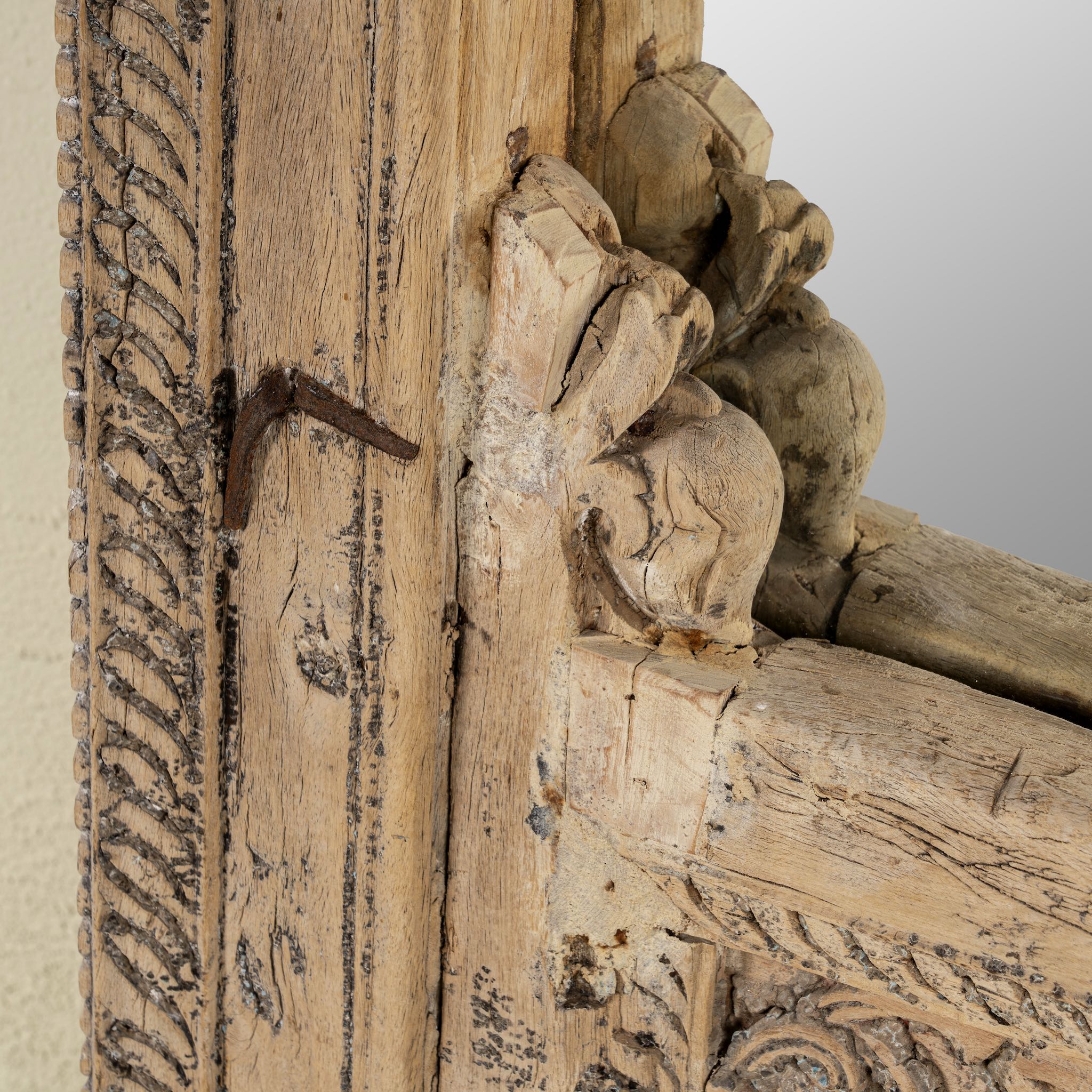 Close up of a hand-carved mirror crafted from an old teak wood window frame, featuring intricate floral and scrollwork details with a natural distressed finish and an arched top design reflecting traditional Indian craftsmanship.
