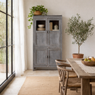 Lifestyle image of a shabby chic teak wood cabinet with glass doors and natural reclaimed finish – sustainable furniture ideal for vintage-style dining and living spaces.