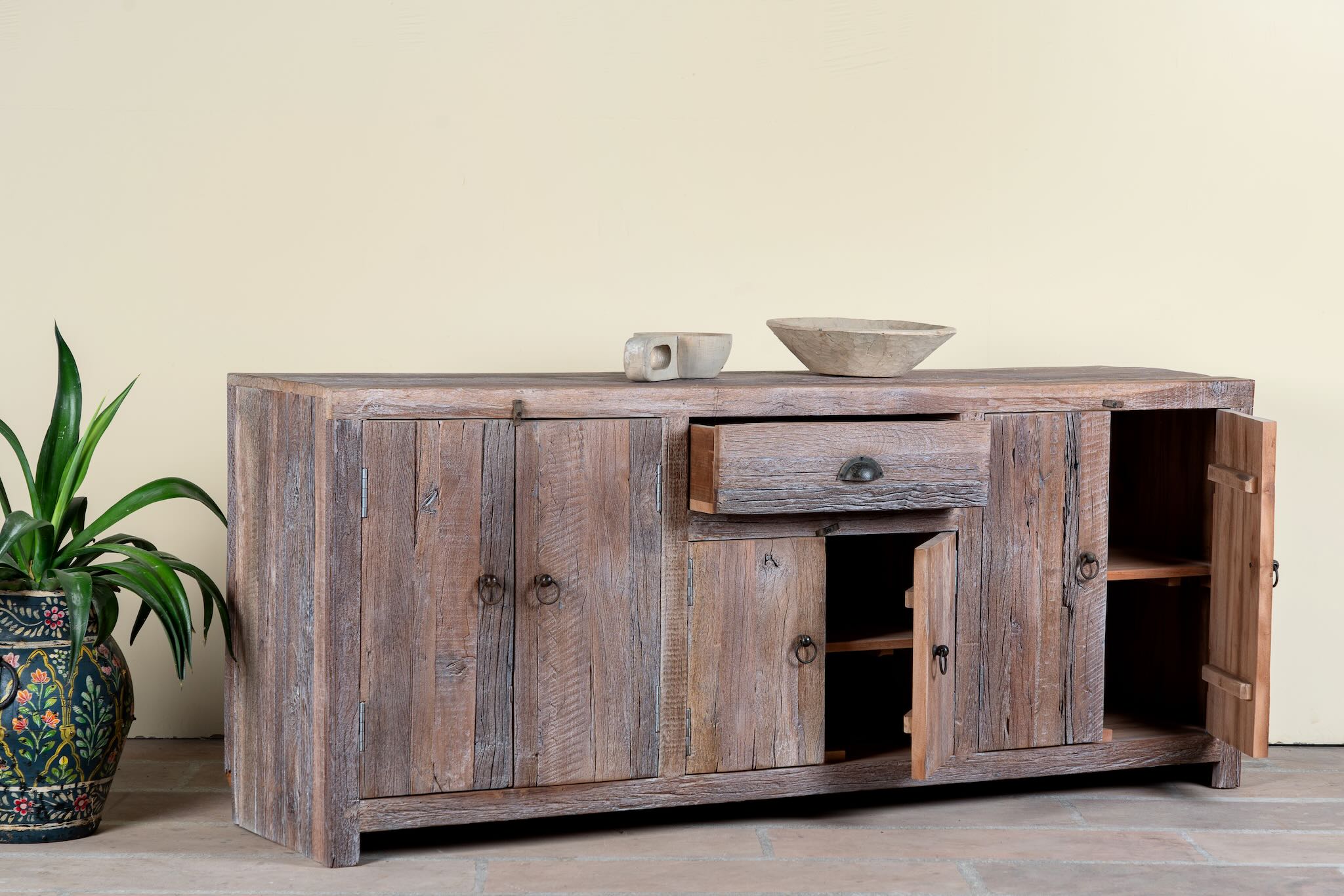 Side angle image with open doors of a reclaimed wood sideboard Devina in rustic minimalistic style with cabinet doors and central drawer. A sustainable furniture piece showcasing natural wood grain and timeless simplicity.