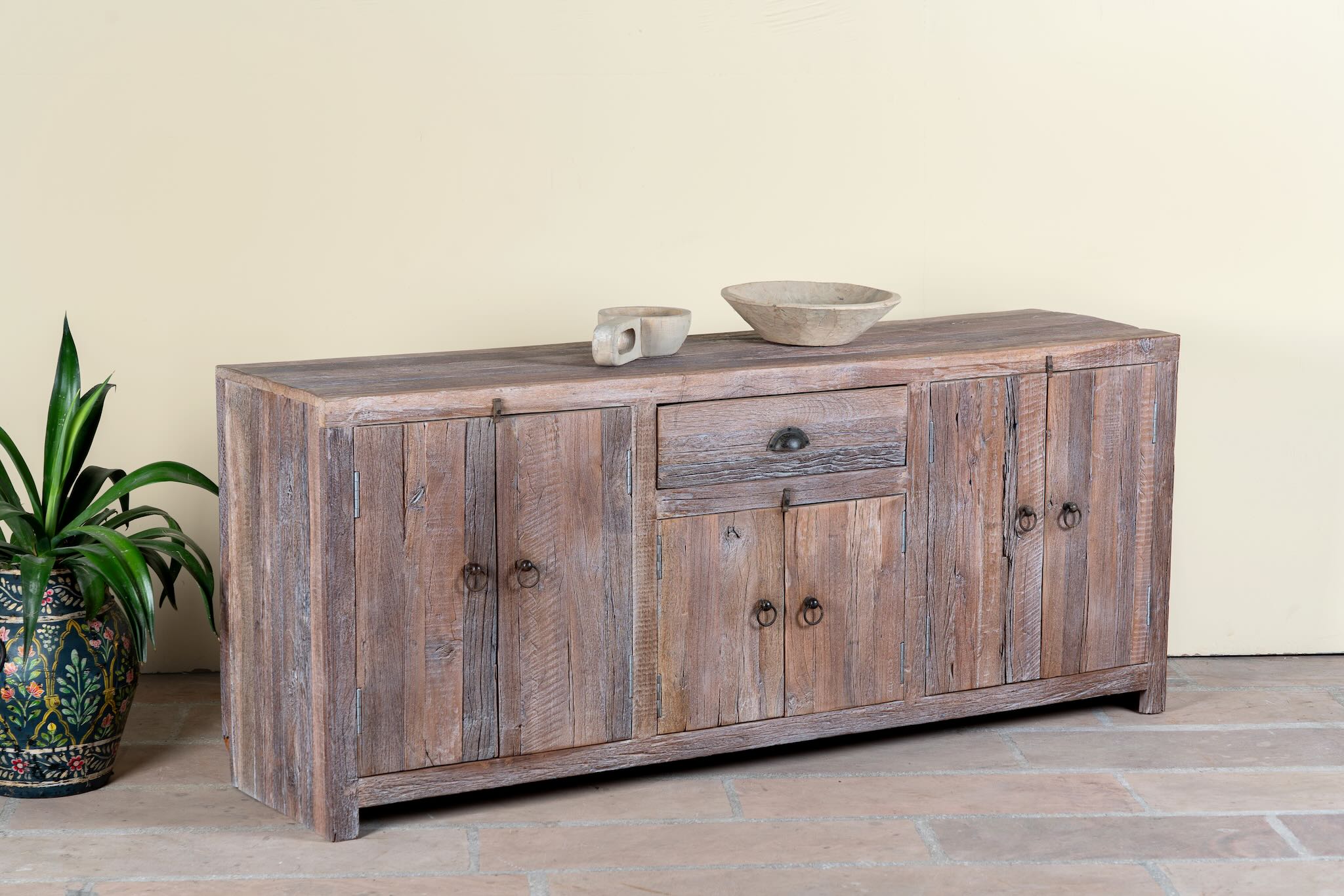 Side angle image of a reclaimed wood sideboard Devina in rustic minimalistic style with cabinet doors and central drawer. A sustainable furniture piece showcasing natural wood grain and timeless simplicity.