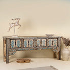 Side angle image of a hand painted console table in reclaimed teak with floral motifs and antique distressed finish, 197 × 40 × 82 cm.