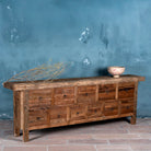 Side view image of a reclaimed wood console table with rustic finish, multiple drawers, and iron ring pulls; sustainable furniture with driftwood charm, 250 × 40 × 85 cm.