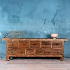 Reclaimed wood console table with rustic finish, multiple drawers, and iron ring pulls; sustainable furniture with driftwood charm, 250 × 40 × 85 cm.