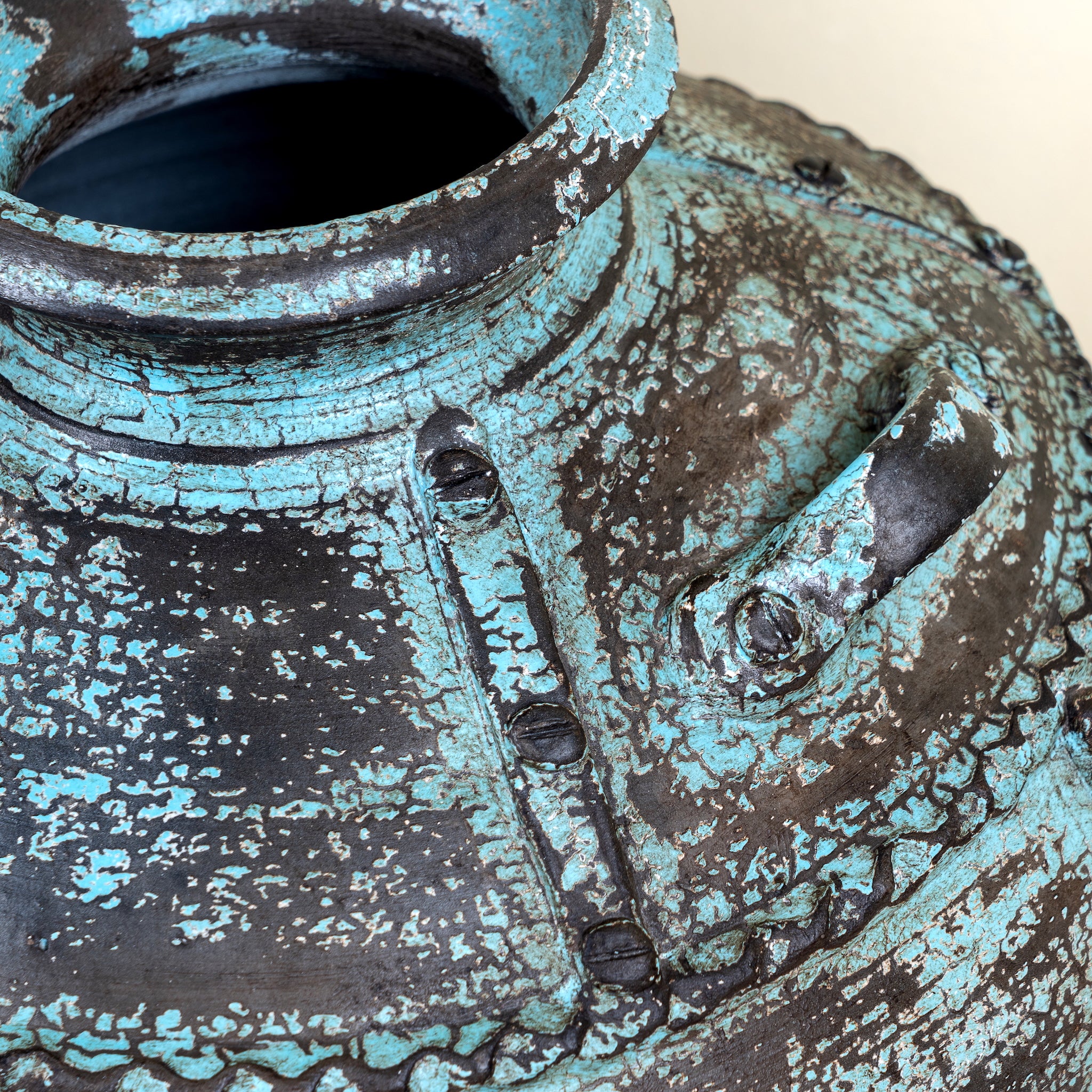 Close up image of a hand-painted clay vase with vintage distressed turquoise finish, sculptural side handles and decorative rivet details, 30x38cm.