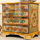 Close up side angle image of a hand-painted reclaimed wood chest of drawers with floral designs and distressed antique finish; perfect for bohemian interiors and vintage hand painted furniture lovers.