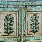 Close up picture of a vintage cabinet made from reclaimed wood, featuring hand-painted floral and tree motifs in vibrant green, red, and turquoise tones for a joyful, artistic touch.