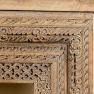 Close up image of a ornate console table crafted from reclaimed teak wood and refurbished architectural elements, featuring intricate hand-carved detailing with floral and geometric motifs, showcasing a vintage artisanal aesthetic.
