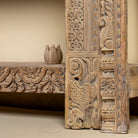 Close up image of a leg design of a  ornate console table crafted from reclaimed teak wood and refurbished architectural elements, featuring intricate hand-carved detailing with floral and geometric motifs, showcasing a vintage artisanal aesthetic.
