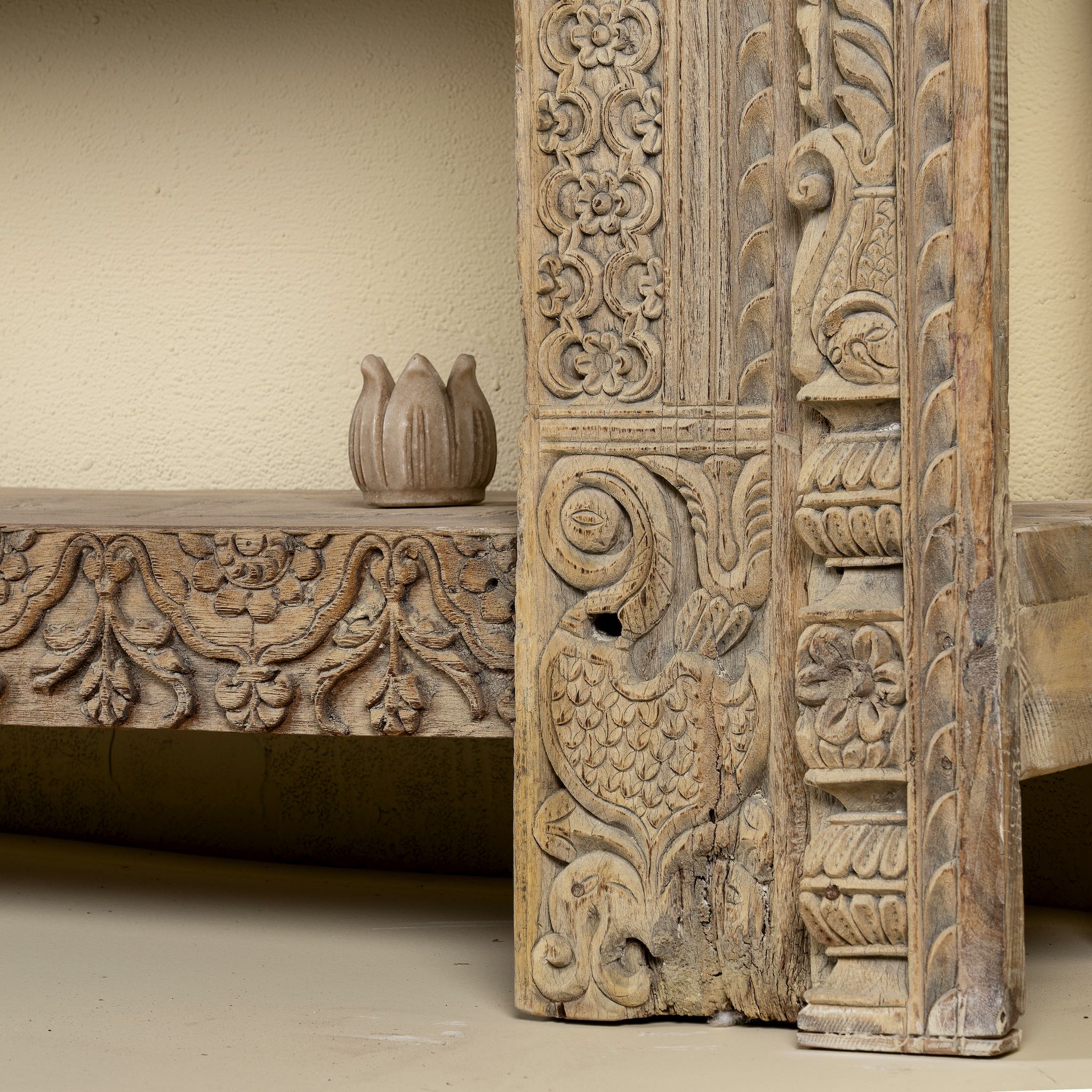 Close up image of a leg design of a  ornate console table crafted from reclaimed teak wood and refurbished architectural elements, featuring intricate hand-carved detailing with floral and geometric motifs, showcasing a vintage artisanal aesthetic.
