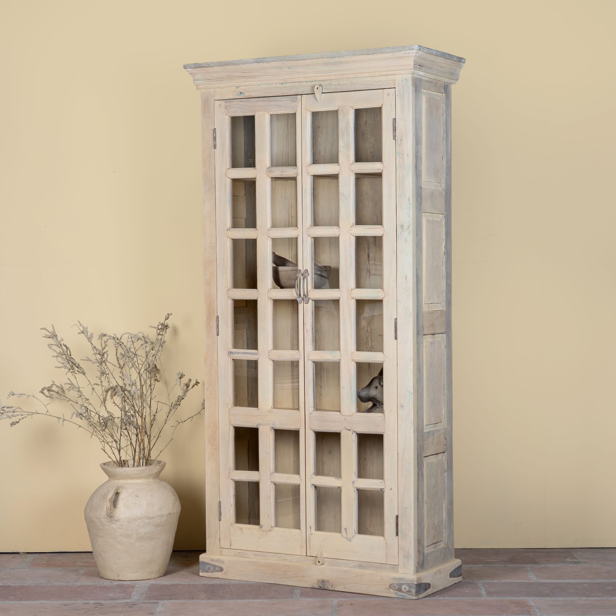 Side angle image of a reclaimed wood display cabinet Eknoor with glass-panelled doors and natural weathered finish. Sustainable living room furniture that can also function as a reclaimed wood wardrobe with spacious shelving.